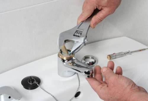 Man repairing a broken faucet or tap on a bathroom sink using a mole grip pliers